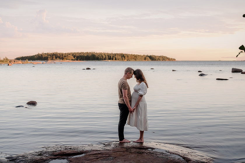 Vauvaa odottava äiti ja isä merenrannalla.