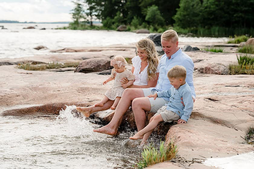 Perhe polskii jaloillaan vettä merenrannalla kallioilla istuen.